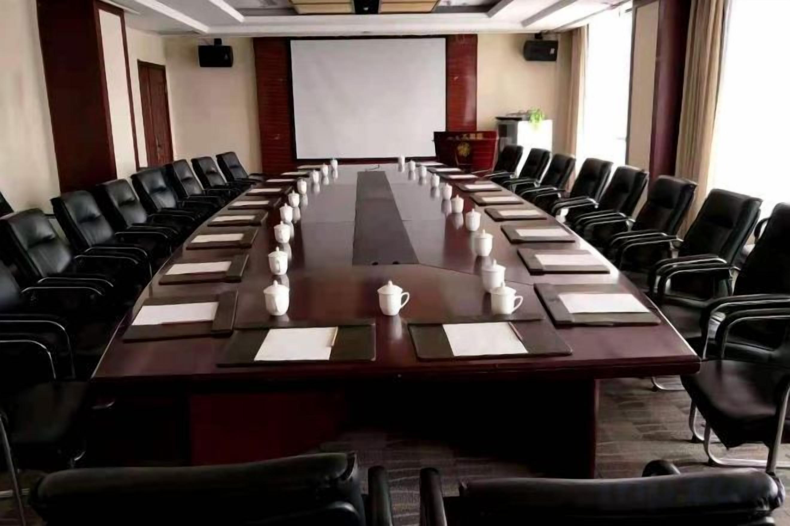 A conference room with a long table, black chairs, and a projector screen.