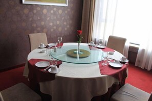 A dining table with a glass top, surrounded by chairs, set with plates, glasses, and a vase with a rose. - Anhua Hotel (Wei County)