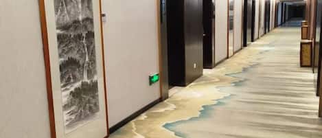 A hallway with a carpet featuring a river design, doors with a green exit sign, and a wall with a framed artwork.