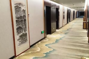 A hallway with a carpet featuring a river design, doors with a green exit sign, and a wall with a framed artwork. - Anhua Hotel (Wei County)