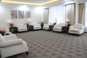 A hotel room with a carpeted floor, white armchairs, a sofa, and a dining table with lamps. There are three paintings on the wall. - Anhua Hotel (Wei County)