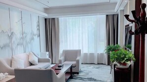 A modern hotel room with a sofa, armchair, coffee table, and a large window with curtains.