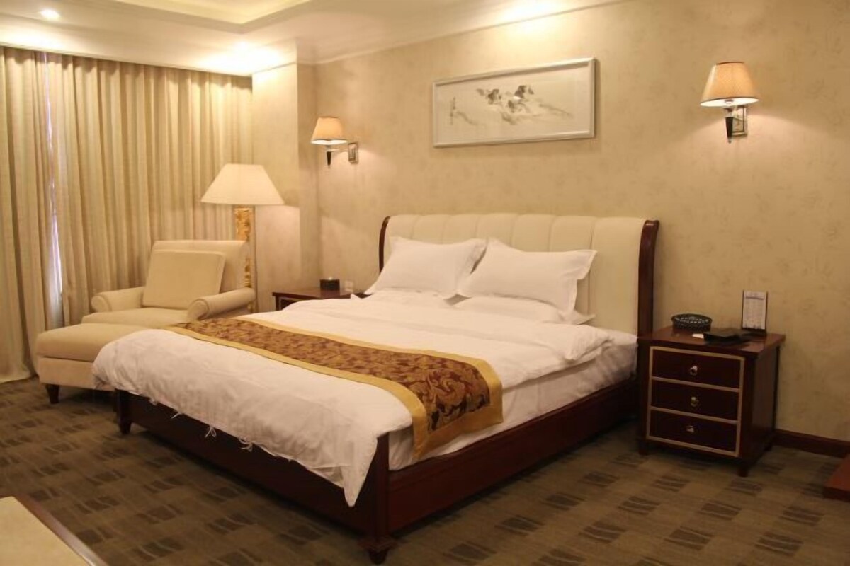 A hotel room with a large bed, a chair, a nightstand, and a lamp.