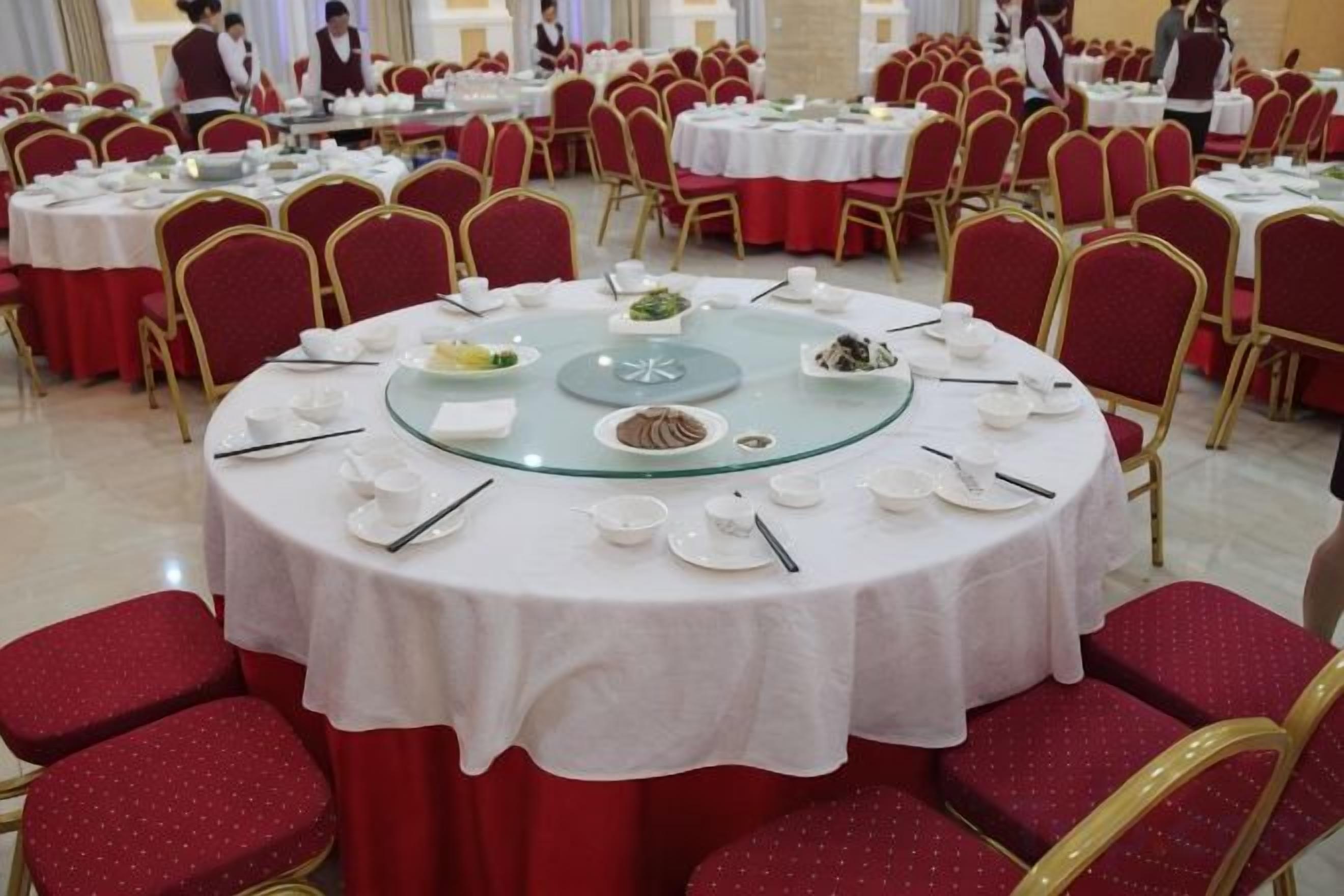 A banquet hall with round tables set for dining, red chairs, and a white tablecloth.