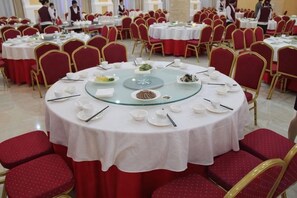 A banquet hall with round tables set for dining, red chairs, and a white tablecloth. - Anhua Hotel (Wei County)