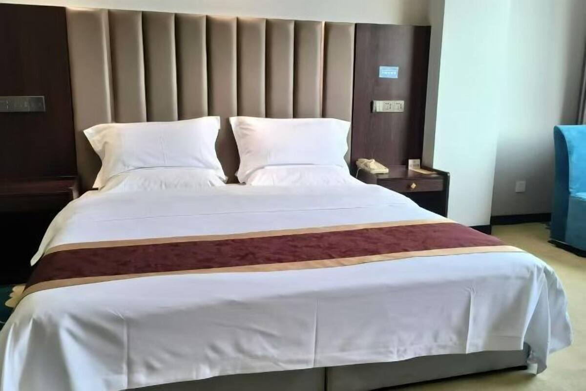 A hotel room with a large bed, a headboard, a bedside table with a phone, and a blue chair.