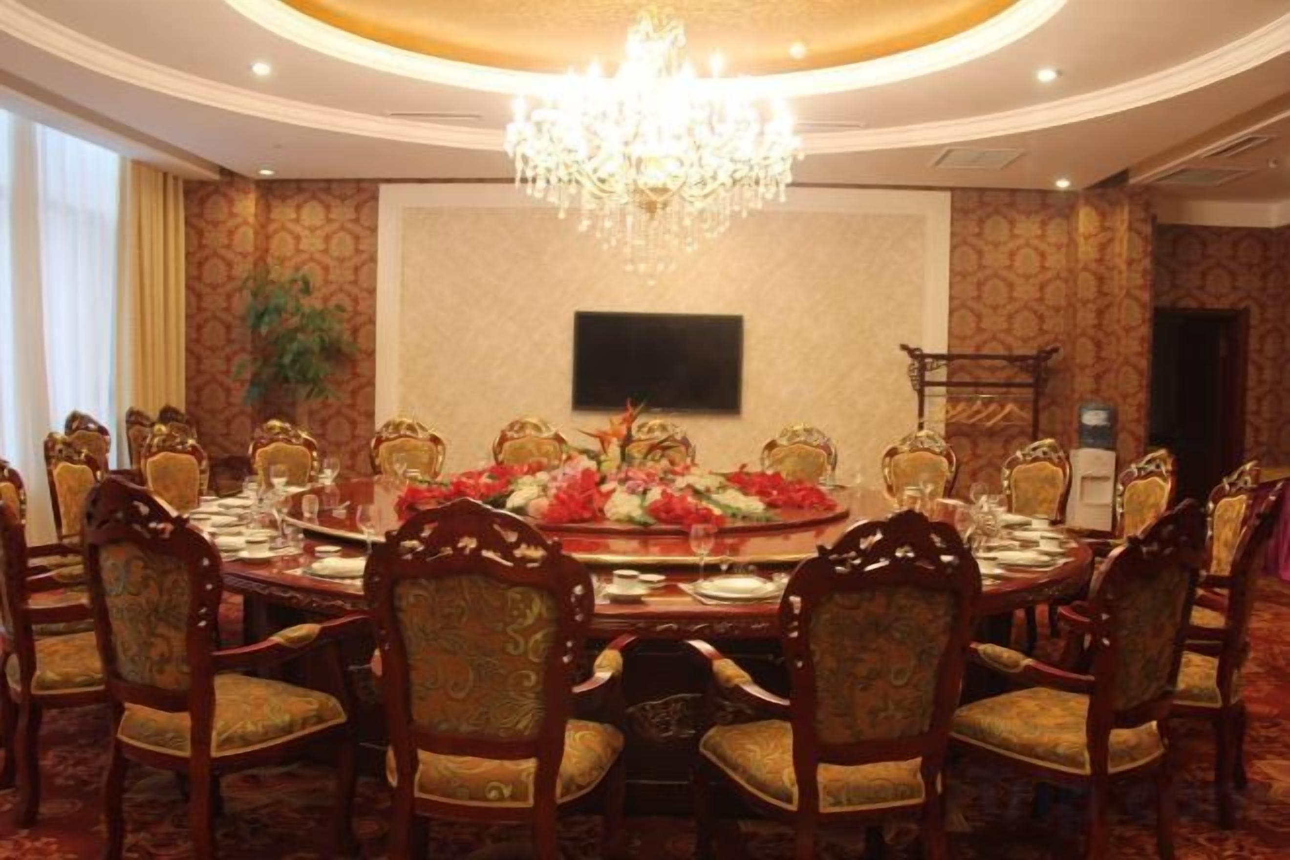 A formal dining room with a round table, ornate chairs, a chandelier, and a television on the wall.