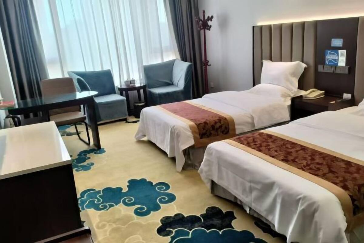 A hotel room with two beds, a desk, a chair, and a coat rack.