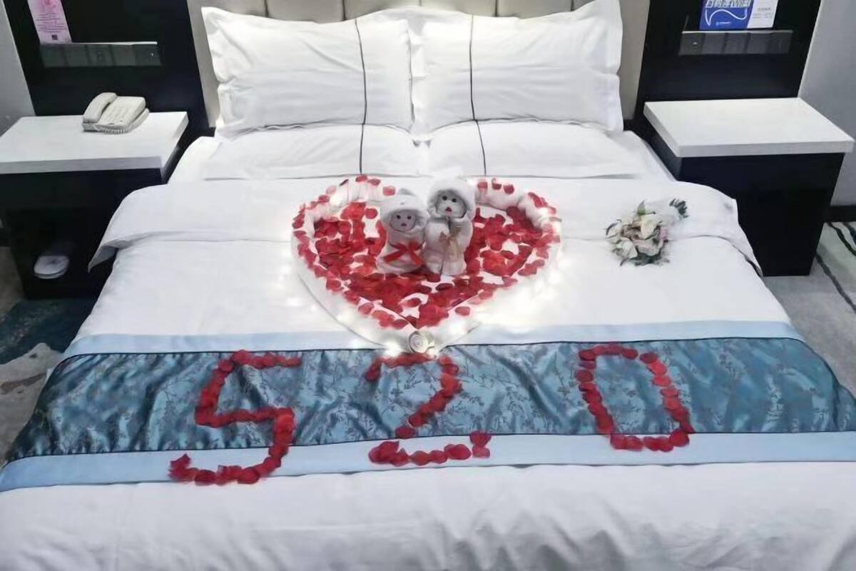 A bed with a heart-shaped arrangement of rose petals and two figurines, a bouquet of flowers, and the numbers "520" on the bedspread.