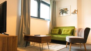 Een woonkamer met een groene bank, een houten salontafel, een grijze fauteuil, een televisie en een lamp.