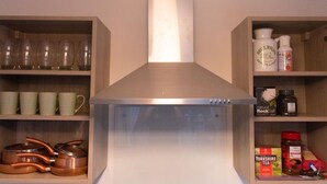 Een keuken met een roestvrijstalen afzuigkap, koperen kookgerei, glazen servies en theezakjes en zout op planken.
