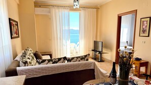 A room with a bed, a TV, a dining table set with plates, glasses, and a vase of flowers. - ERAL Apart-Hotel (Sarandë)