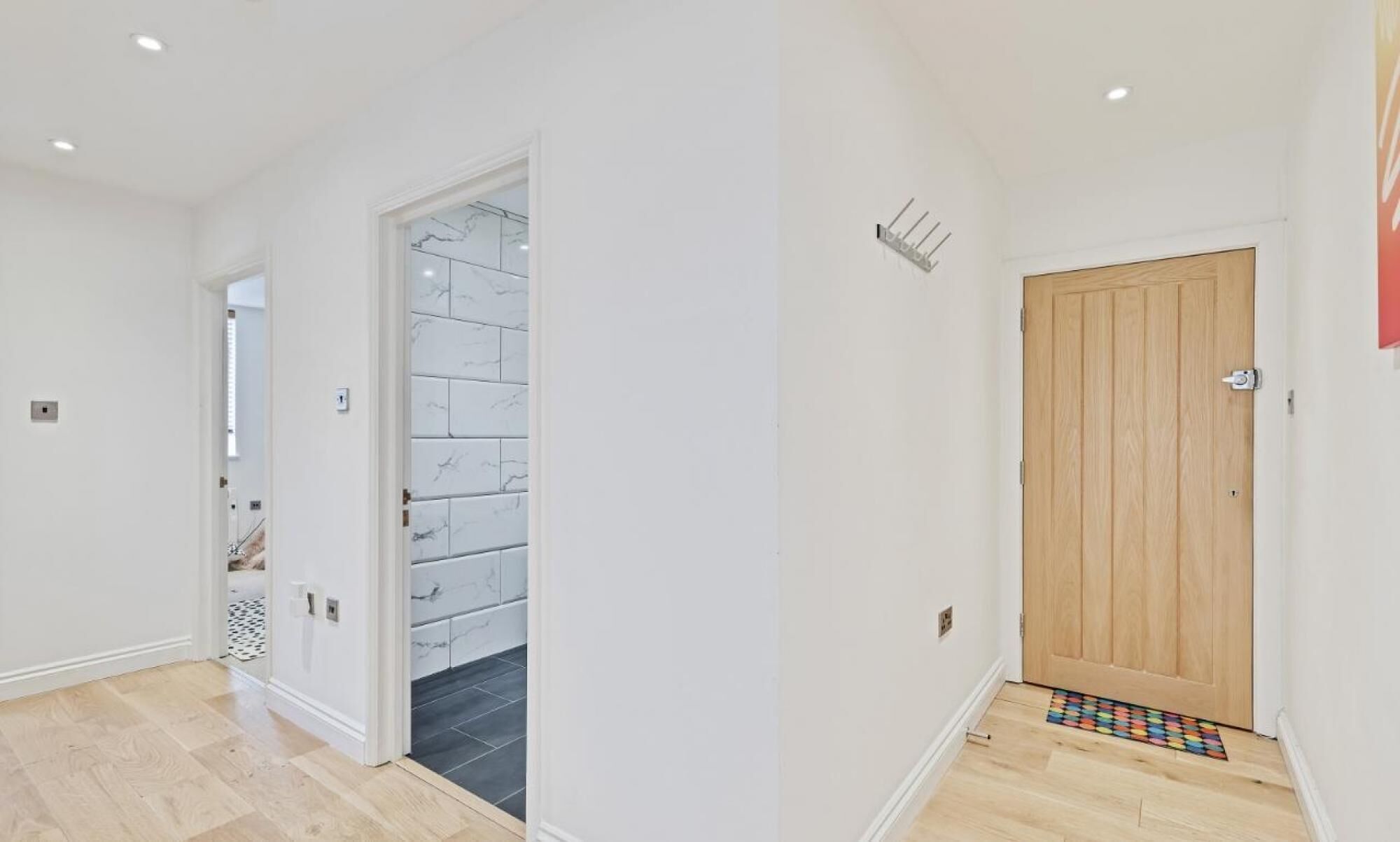 Un couloir avec une porte en bois, un mur recouvert de carreaux et un interrupteur sur le mur.