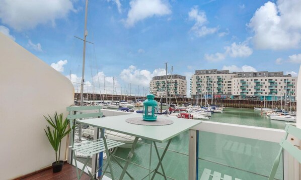 A balcony with a view of a marina, a potted plant, and a teal lantern.