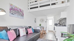 Um apartamento moderno com um sofá cinzento, almofadas coloridas, um tapete com bolinhas, área de refeições e cozinha compacta.