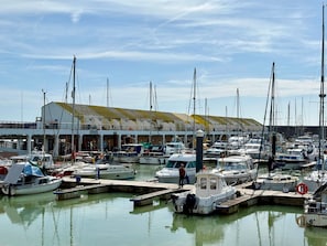 A marina with multiple boats docked, a building with a flat roof, and a person standing on the dock.