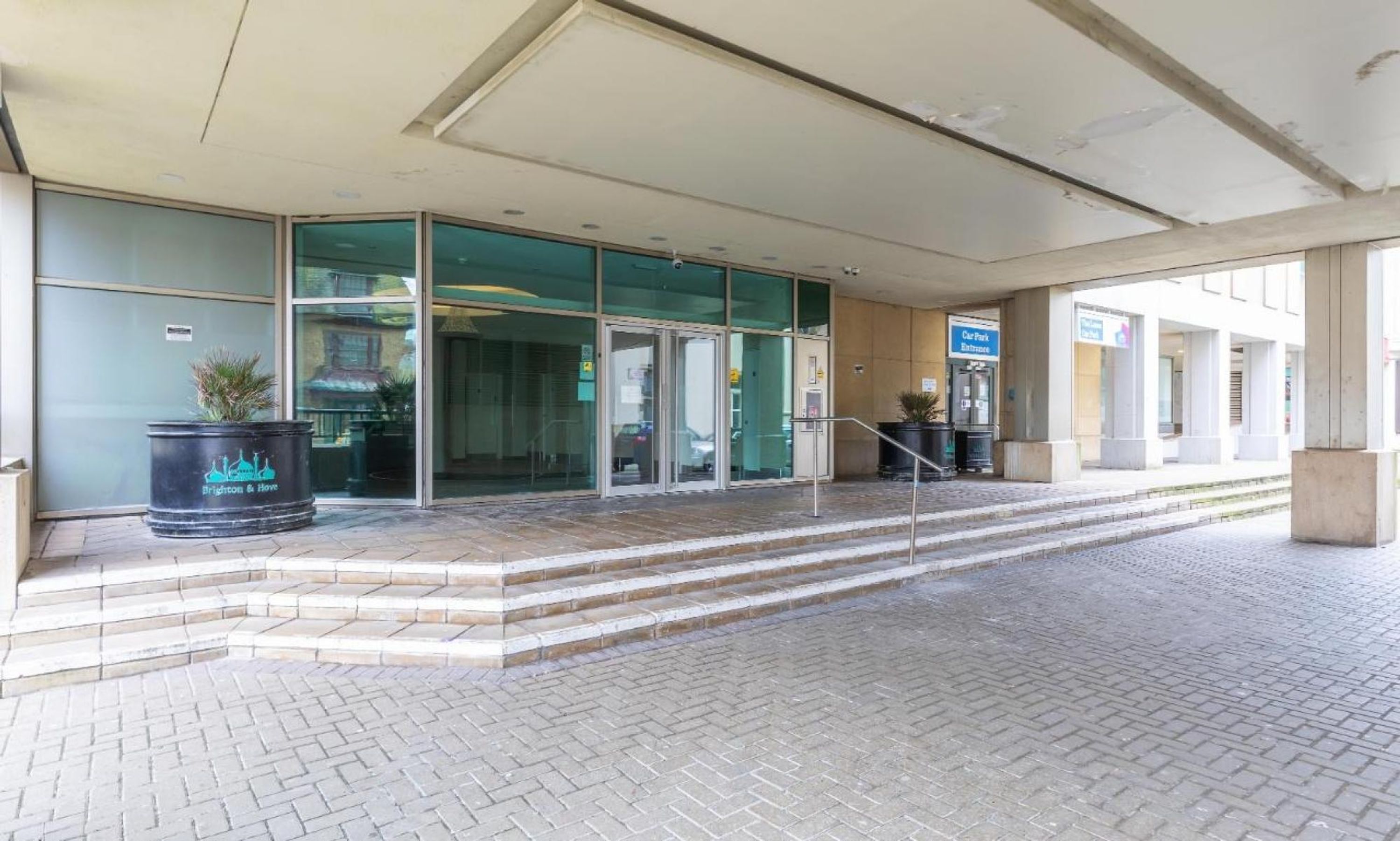 A building entrance with a glass door, a car park sign, and a staircase leading up to the entrance.