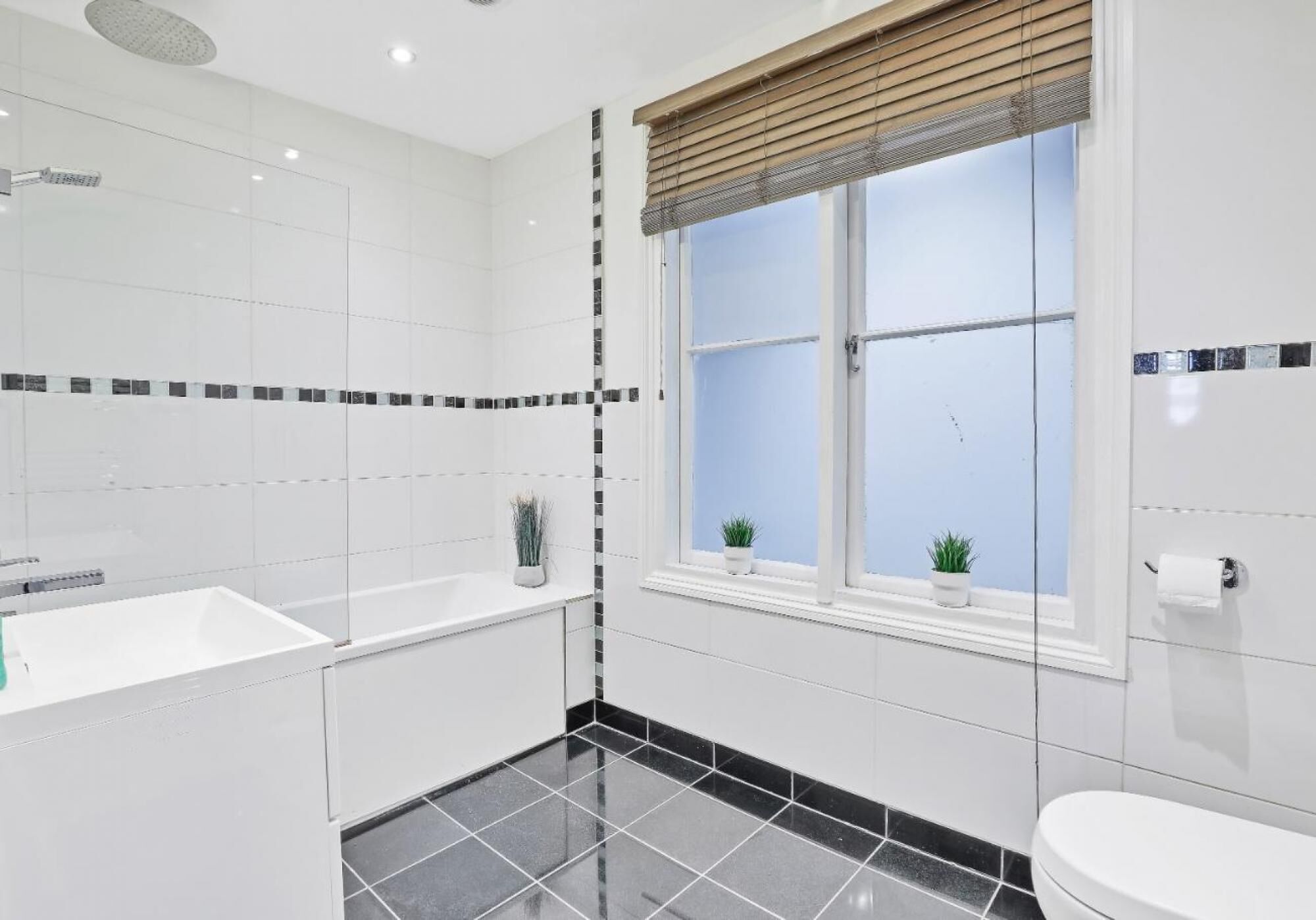 Un baño moderno con bañera, inodoro y ventana con persianas.