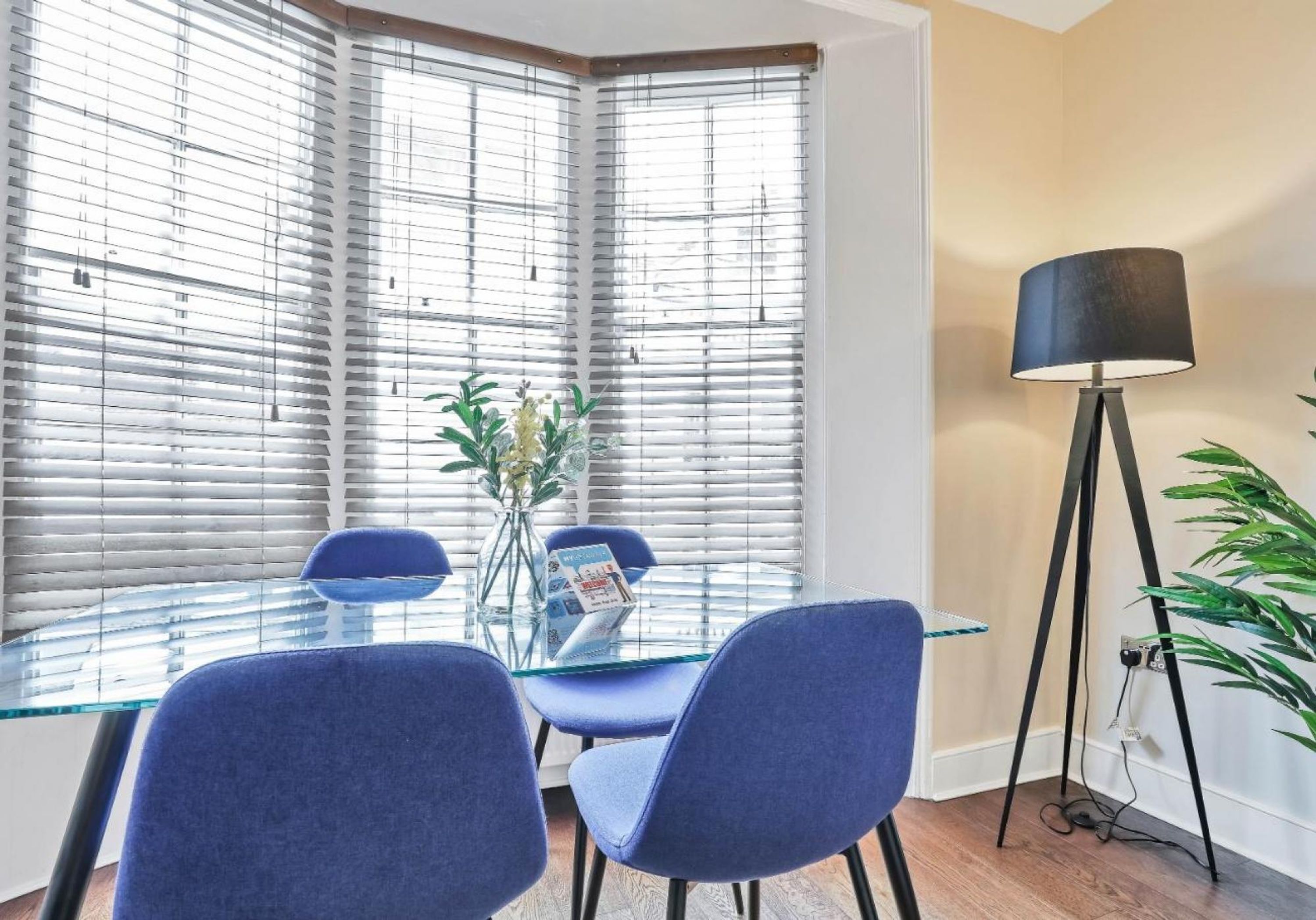 Un comedor moderno con una mesa de vidrio, sillas azules y un jarrón con flores.