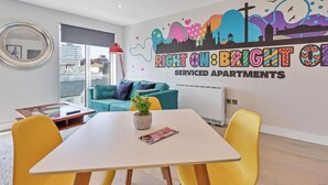 A modern living room with a white table, yellow chairs, a teal sofa, and a colorful mural on the wall.