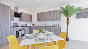 A modern kitchen with grey cabinets, a built-in oven, and a dining area with yellow chairs and a white table set for four.