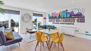 Una sala de estar moderna con un sofá, una mesa de comedor con sillas amarillas y un ventanal con vistas a la ciudad.