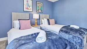 Una habitación de hotel con dos camas, una mesita de noche con lámpara y dos cuadros enmarcados en la pared.