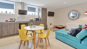 A modern kitchen with a built-in oven and microwave, a dining area with yellow chairs, and a blue sofa with cushions. - Right On Bright On Apartment 1G - City Centre Luxury Apartments (Brighton)