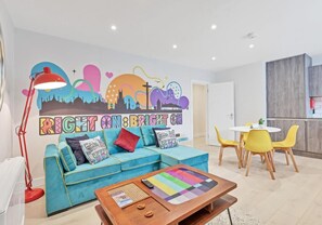 A modern living room with a teal sofa, a wooden coffee table, and a colorful wall mural. - Right On Bright On Apartment 1G - City Centre Luxury Apartments (Brighton)