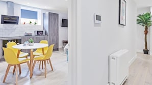 A modern kitchen with white cabinets, a built-in oven, and a dining area with yellow chairs. - Right On Bright On Apartment 1G - City Centre Luxury Apartments (Brighton)