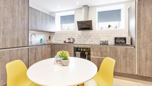 A modern kitchen with wooden cabinets, a built-in oven, and a dining area with yellow chairs. - Right On Bright On Apartment 1G - City Centre Luxury Apartments (Brighton)
