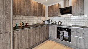 A modern kitchen with wooden cabinets, a microwave, a toaster, and a dishwasher. - Right On Bright On Apartment 1E - City Centre Luxury Apartments (Brighton)