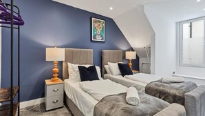 A bedroom with two beds, a ceiling fan, a painting, and a window. - Right On Bright On Apartment 1E - City Centre Luxury Apartments (Brighton)