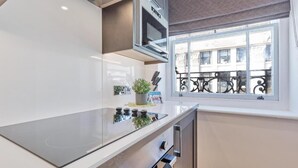 Une cuisine compacte équipée d’un micro-ondes encastré, d’une petite plante en pot et d’une fenêtre donnant sur un immeuble.