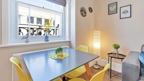 Un espace repas comprenant une table et des chaises, une fenêtre donnant sur des immeubles et des œuvres d’art décoratives sur les murs.