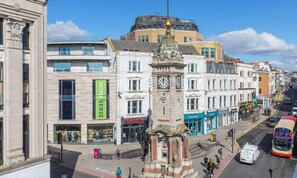 A street view with a prominent clock tower, a Superdry store, and a bus stop.
