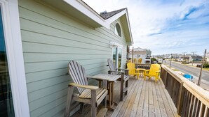 Een houten terras met Adirondack-stoelen en een gele stoel, met uitzicht op een straat.