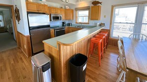 Een moderne keuken met houten kastjes, roestvrijstalen apparatuur, een groot eiland met barstoelen en uitzicht op de stad door het raam.