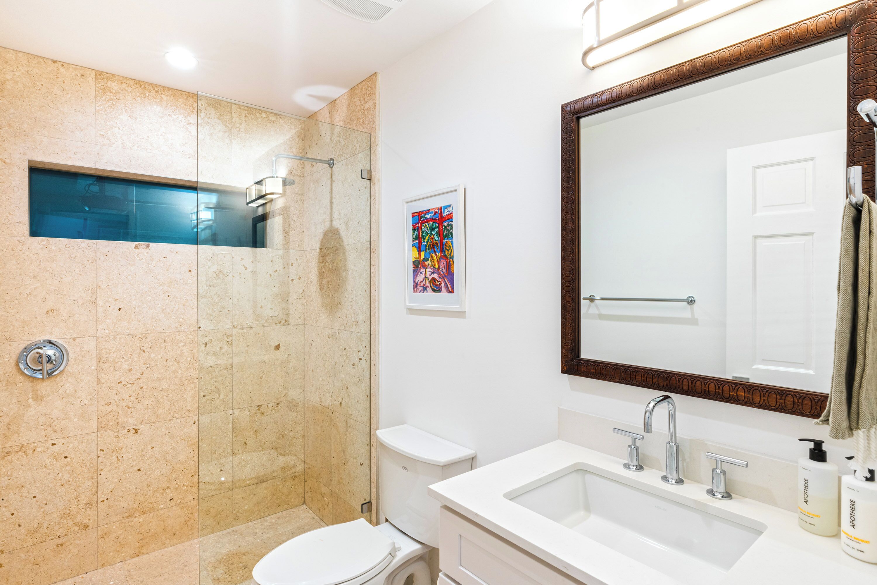 A modern bathroom with a glass-enclosed shower, a white toilet, a large mirror, and a sink with toiletries.