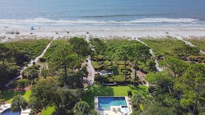 Vista aérea de una propiedad costera con piscina, jardín ajardinado y una playa al fondo.