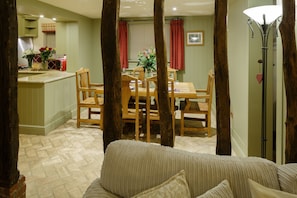 A cozy living room with a sofa, a dining table with chairs, and a kitchen area in the background. - LUXURY: JACUZZI, SAUNA, FIREPLACE, DOGS WELCOME (Stoke Ash)