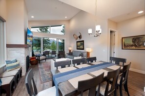 Uma sala de jantar espaçosa com uma mesa comprida, várias cadeiras e vista para o exterior através de grandes janelas.