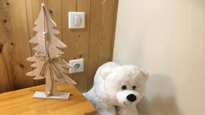 Ein weißer Teddybär neben einem Holztisch mit einer kleinen Weihnachtsbaumdekoration.