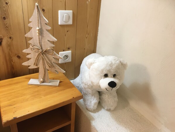 Ein weißer Teddybär neben einem Holztisch mit einer kleinen Weihnachtsbaumdekoration.