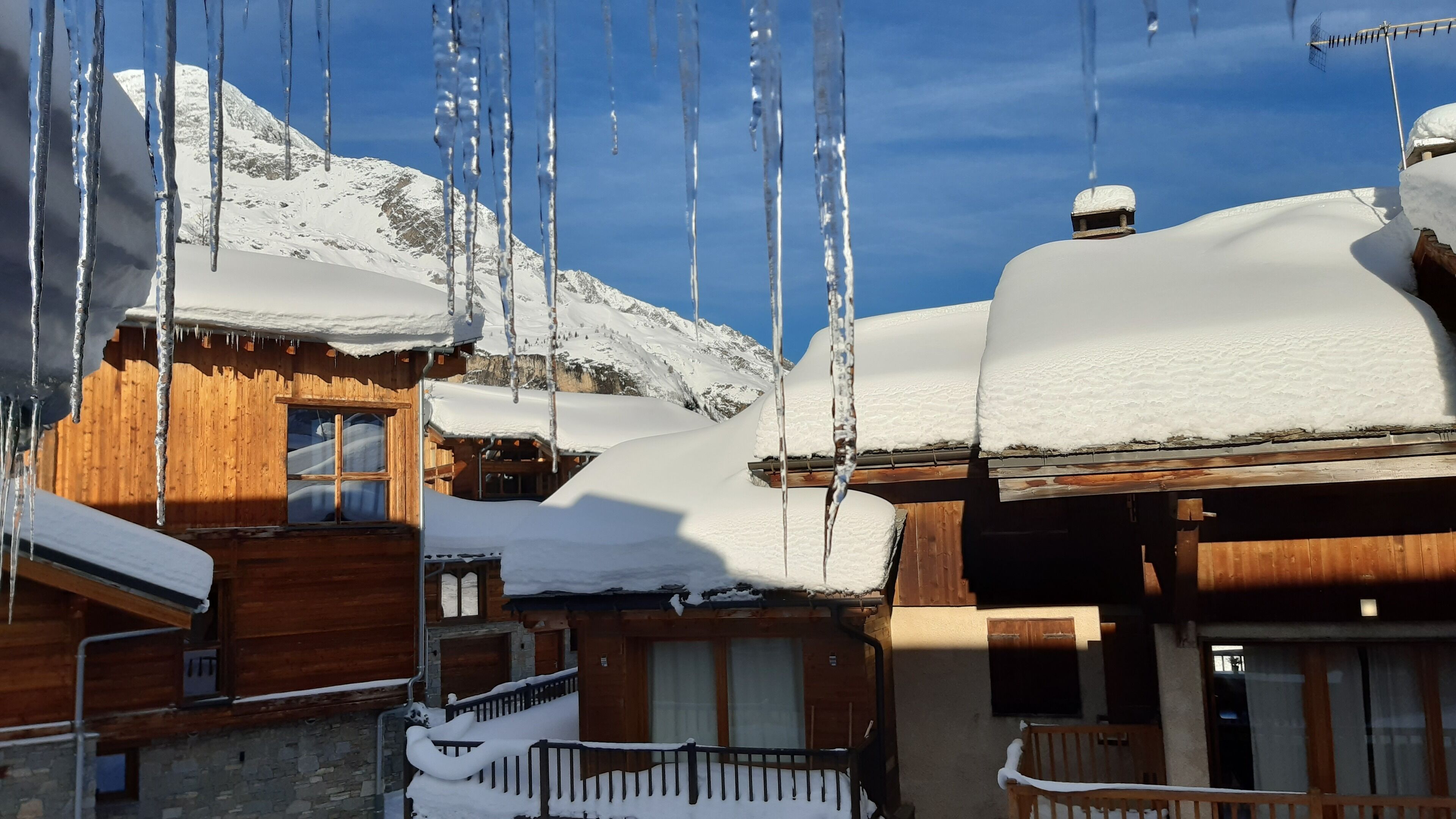 Un chalet en bois, dont les toits sont recouverts de neige et des glaçons pendent des avant-toits.
