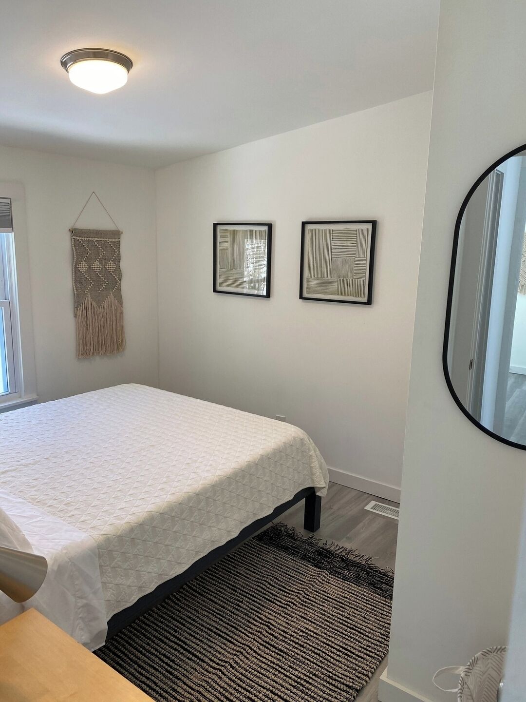 Un dormitorio con una cama, un adorno de macramé en la pared y dos cuadros enmarcados.