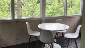 Una habitación con una mesa redonda y cuatro sillas, ventanas amplias con vistas a zonas verdes y un ventilador de techo.