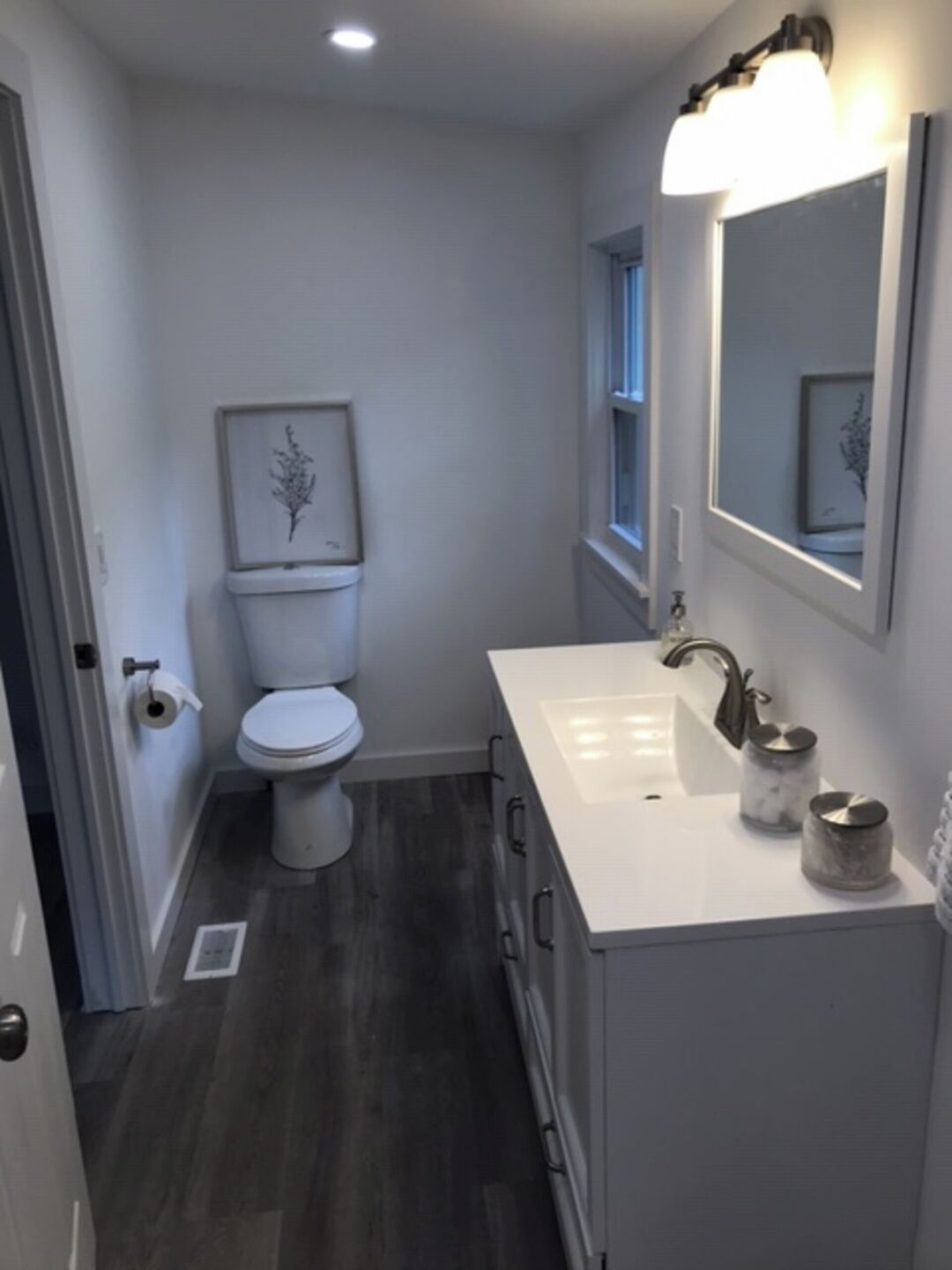 A compact bathroom with a white toilet, a white sink with a mirror above it, and a small window.