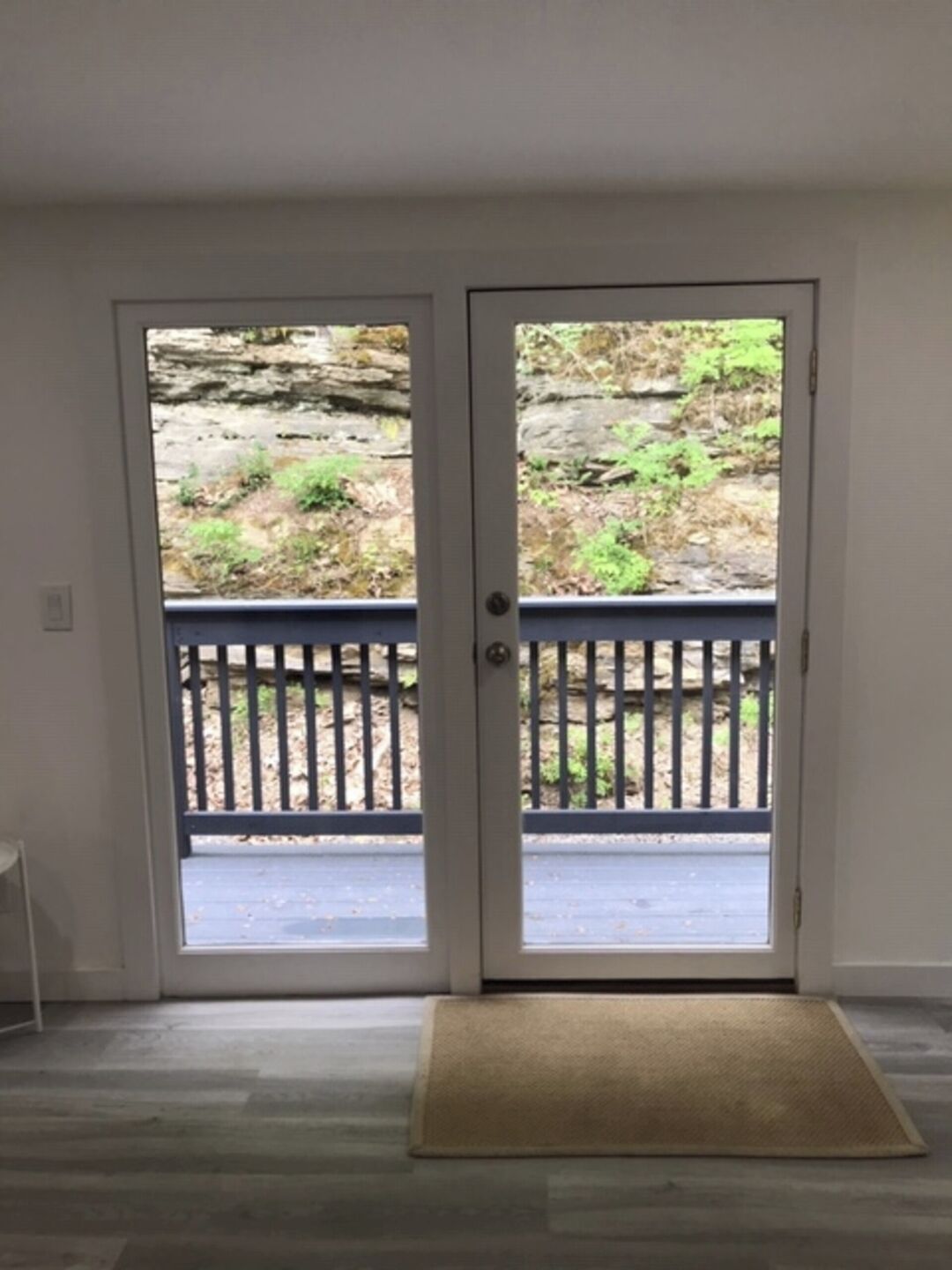 A room with a double door leading to an outdoor area with a wooden deck and a stone wall.