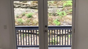 Una habitación con un par de puertas que dan a un espacio exterior con terraza de madera y pared de piedra.